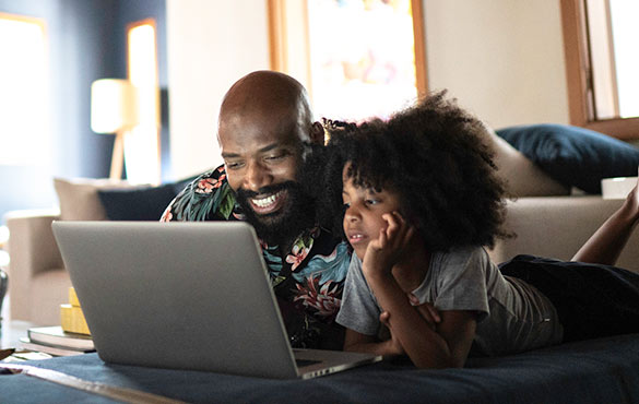 Father and daughter using laptop on couch.